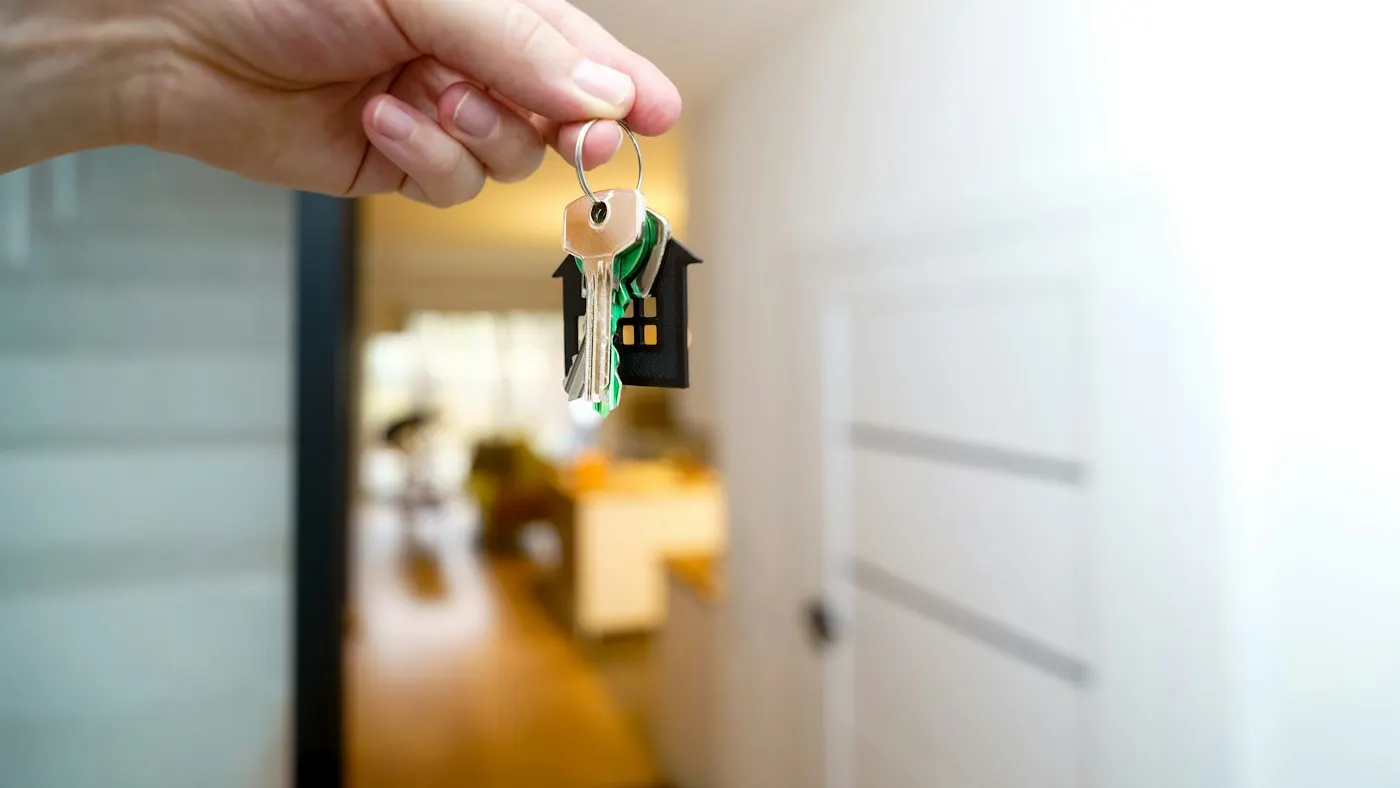 Mão segurando um chaveiro em formato de casa na entrada de um imóvel